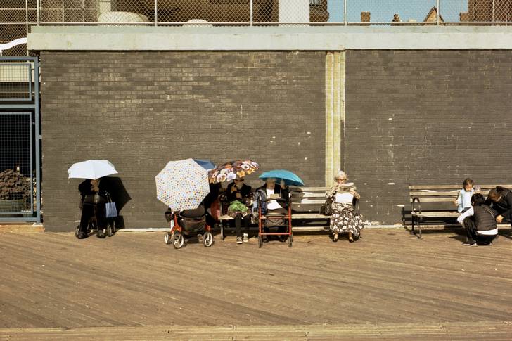 people with umbrellas sit on the Brighton Beach boardwalk